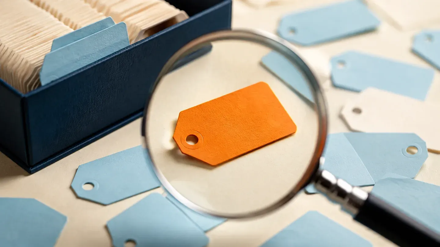 A magnifying glass isolates an orange tag among blank cream and blue tags.